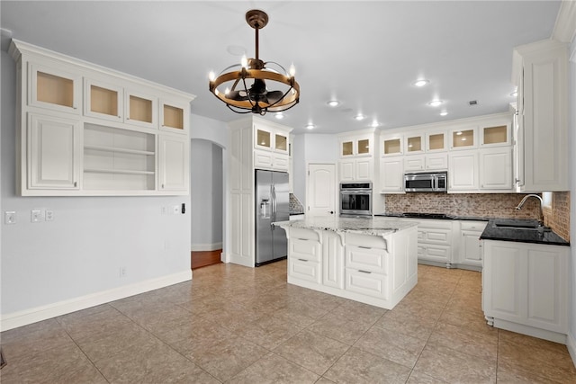 kitchen with decorative backsplash, stainless steel appliances, arched walkways, white cabinetry, and a sink