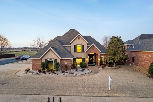 traditional-style house featuring stucco siding, brick siding, and a shingled roof