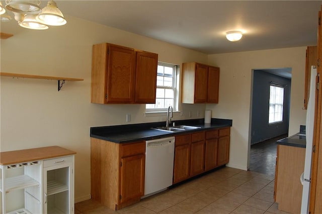 kitchen with light tile patterned floors, brown cabinetry, dishwasher, dark countertops, and a sink