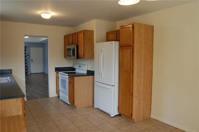 kitchen with light tile patterned floors, white appliances, dark countertops, and a sink