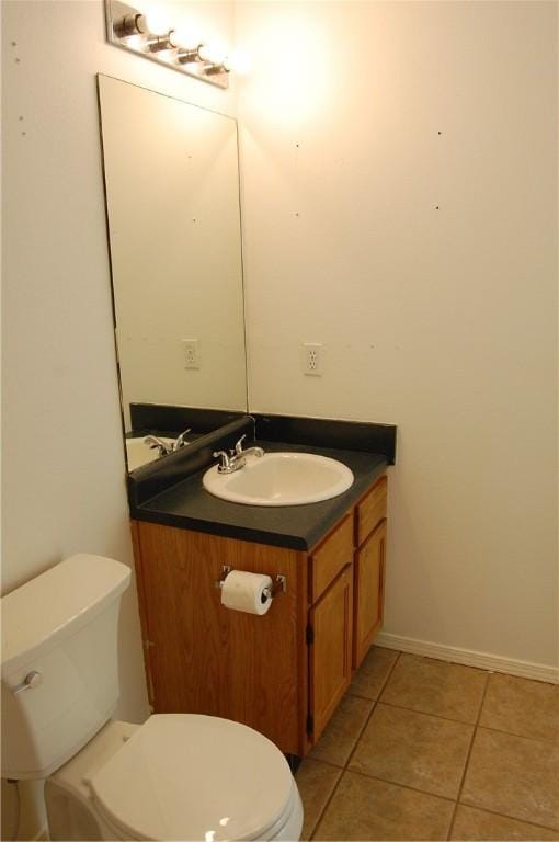 half bathroom featuring tile patterned flooring, baseboards, vanity, and toilet