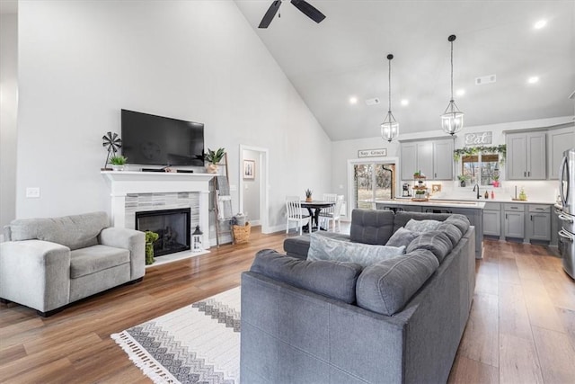 living room featuring high vaulted ceiling, a tile fireplace, wood finished floors, visible vents, and a ceiling fan