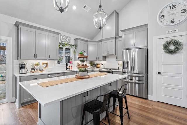 kitchen with lofted ceiling, stainless steel appliances, visible vents, light wood-type flooring, and gray cabinets