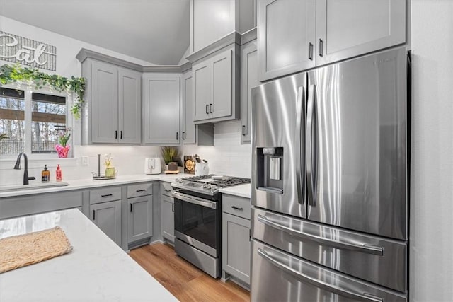 57 Cromarty Dr, Bella Vista, AR 72715 - kitchen featuring appliances with stainless steel finishes, gray cabinetry, a sink, light wood-style flooring, and vaulted ceiling