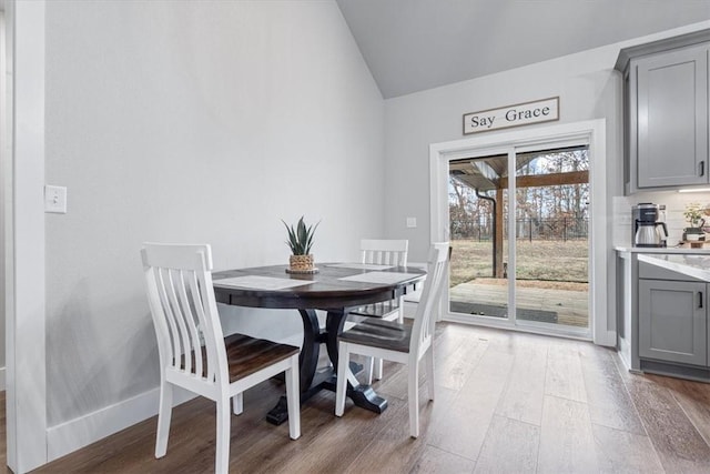 dining area featuring lofted ceiling, light wood-style flooring, and baseboards