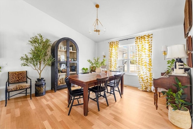 dining space featuring vaulted ceiling, light wood finished floors, and an inviting chandelier