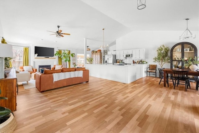 living area with plenty of natural light, light wood-style flooring, vaulted ceiling, and a glass covered fireplace