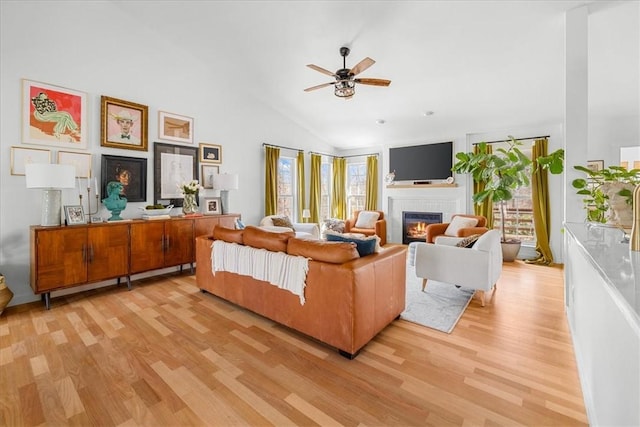 living area with ceiling fan, high vaulted ceiling, light wood-type flooring, and a glass covered fireplace