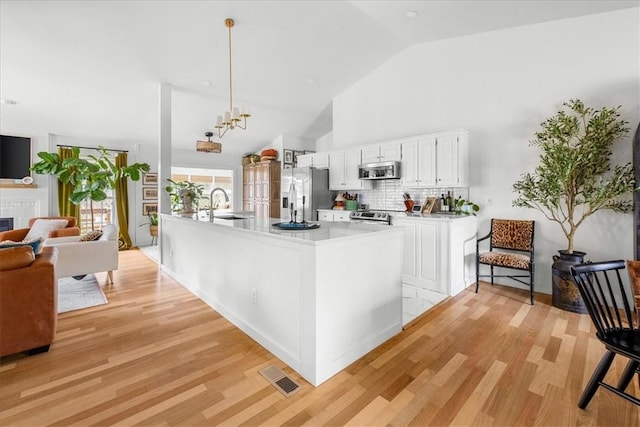 kitchen with stainless steel appliances, light countertops, visible vents, a tiled fireplace, and a sink