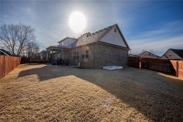 rear view of property with a trampoline, a yard, a fenced backyard, and brick siding