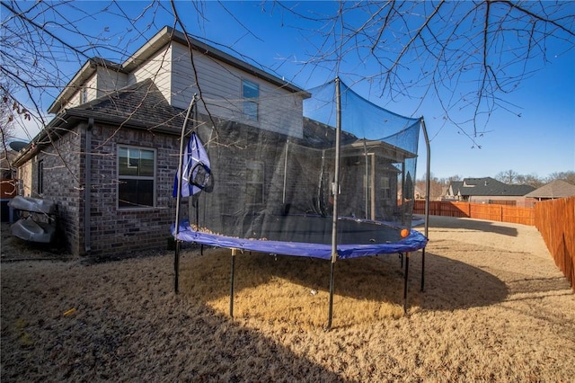 back of house featuring a fenced backyard, a trampoline, and brick siding