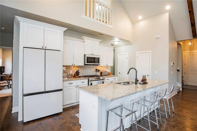 kitchen with an island with sink, white appliances, white cabinets, and a sink