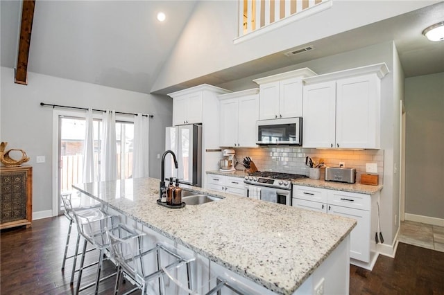 kitchen featuring visible vents, decorative backsplash, a kitchen island with sink, stainless steel appliances, and a sink