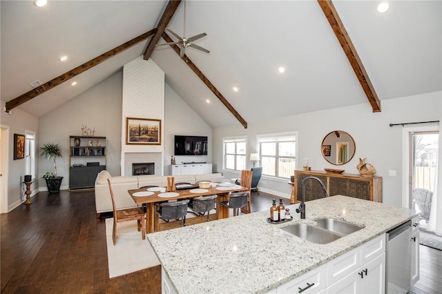 kitchen with beam ceiling, a fireplace, open floor plan, a sink, and dishwasher