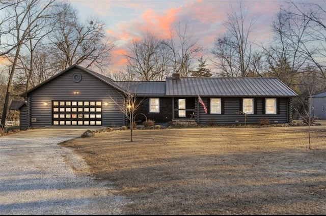 view of front of house featuring a chimney, an attached garage, a standing seam roof, metal roof, and driveway