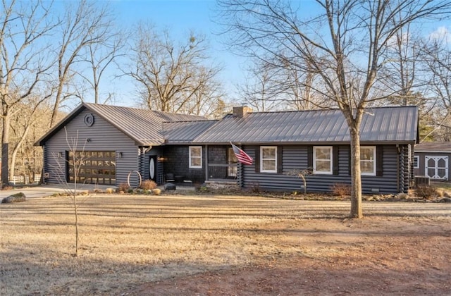 view of front facade with metal roof, a garage, concrete driveway, log siding, and a chimney