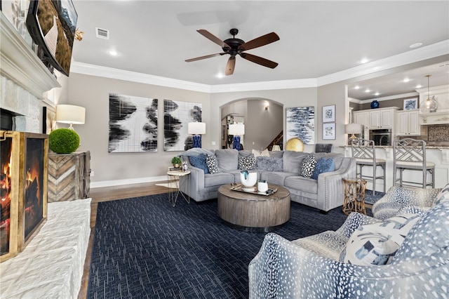 living area with arched walkways, a warm lit fireplace, visible vents, and crown molding