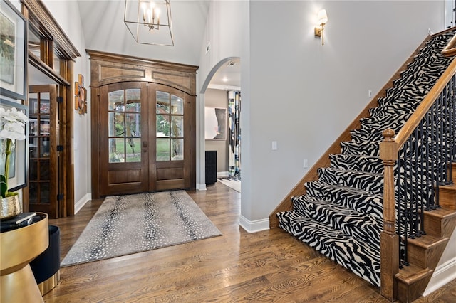 entryway featuring arched walkways, a high ceiling, wood finished floors, stairs, and french doors