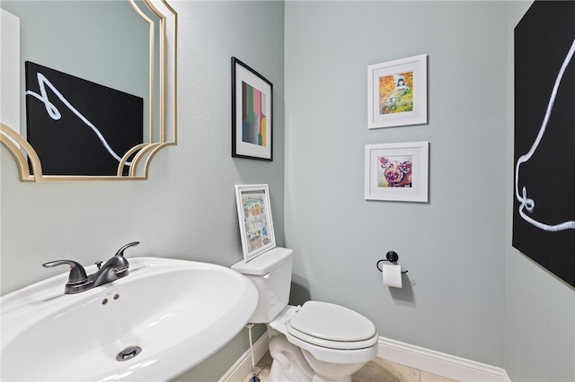 half bathroom featuring tile patterned flooring, baseboards, a sink, and toilet