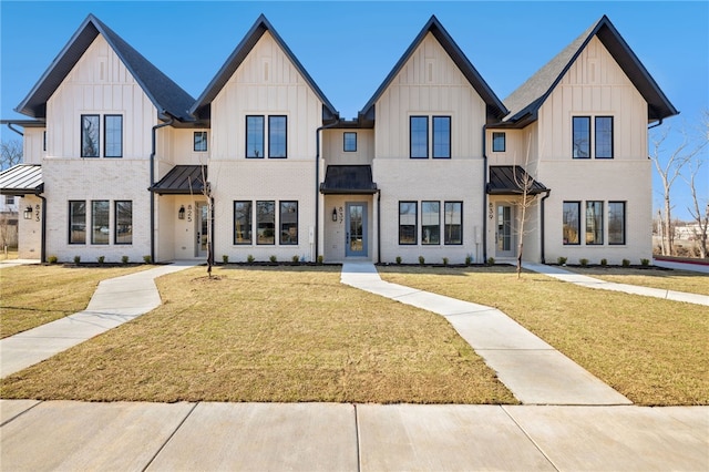 modern farmhouse featuring a standing seam roof, brick siding, board and batten siding, and a front yard