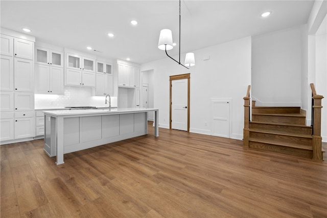 kitchen with light countertops, white cabinetry, a sink, an island with sink, and wood finished floors