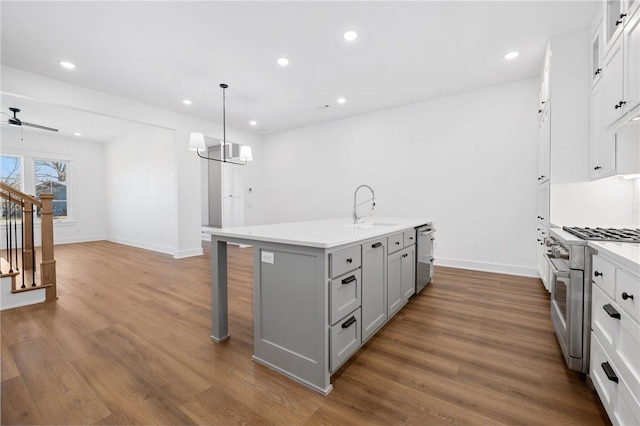 kitchen featuring a center island with sink, gray cabinets, appliances with stainless steel finishes, dark wood-type flooring, and a sink