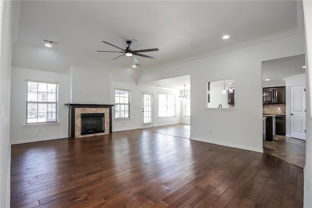 unfurnished living room featuring ceiling fan with notable chandelier, dark wood-style flooring, a tile fireplace, and baseboards