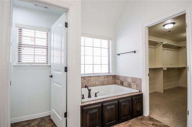 bathroom featuring a walk in closet, a garden tub, plenty of natural light, and visible vents