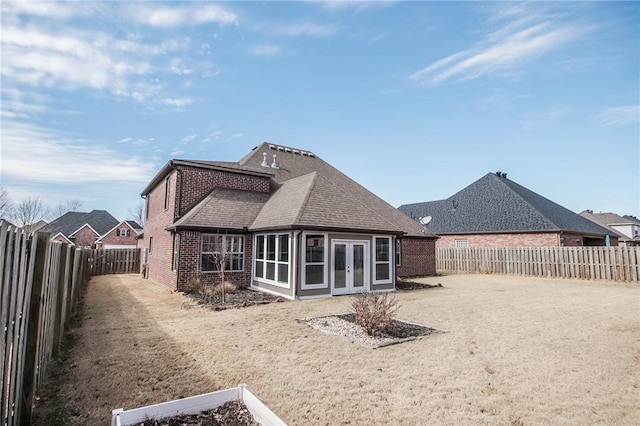 rear view of property with brick siding, a fenced backyard, a shingled roof, and french doors