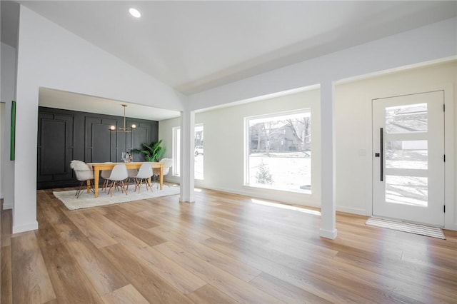 unfurnished living room featuring baseboards, light wood-style flooring, an inviting chandelier, vaulted ceiling, and ornate columns