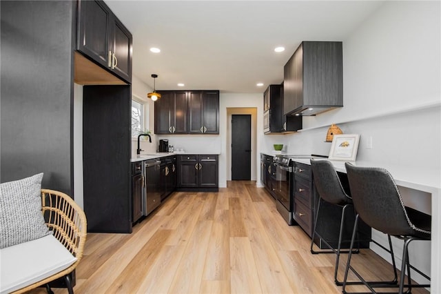 kitchen featuring light wood finished floors, wall chimney exhaust hood, stainless steel appliances, light countertops, and a sink