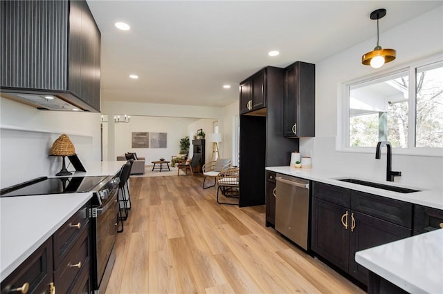 kitchen with light countertops, appliances with stainless steel finishes, a sink, wall chimney range hood, and light wood-type flooring