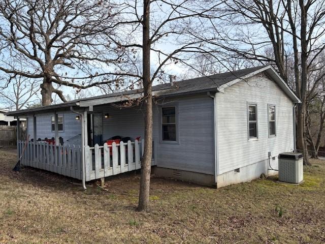 view of side of property with crawl space, a lawn, fence, and central AC unit