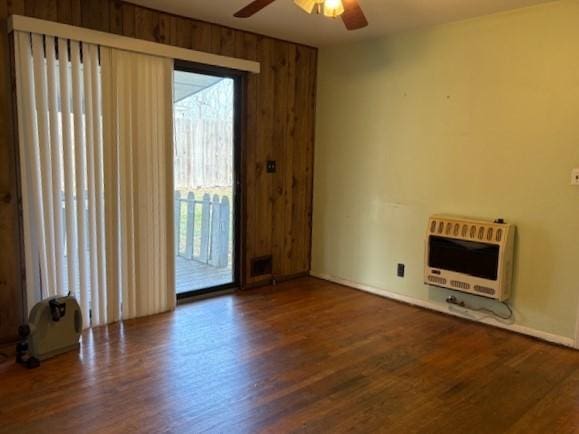 unfurnished living room featuring wood walls, wood finished floors, a ceiling fan, and heating unit