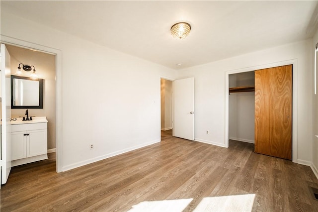 unfurnished bedroom with a closet, connected bathroom, a sink, wood finished floors, and baseboards