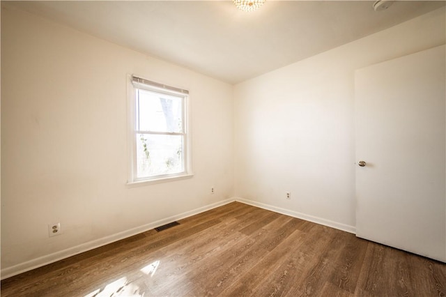 empty room with baseboards, visible vents, and wood finished floors