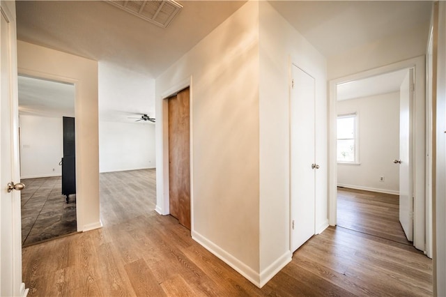 hall with visible vents, baseboards, and wood finished floors