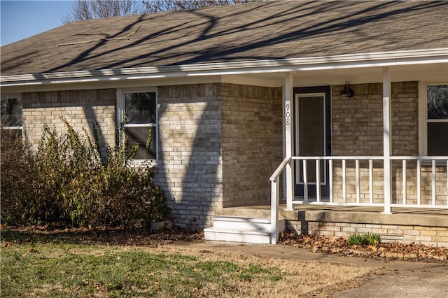 view of exterior entry with roof with shingles and brick siding