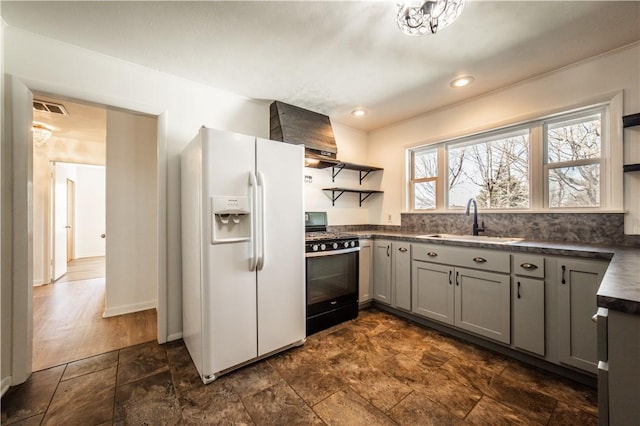 kitchen with black range with gas cooktop, white refrigerator with ice dispenser, gray cabinets, open shelves, and dark countertops