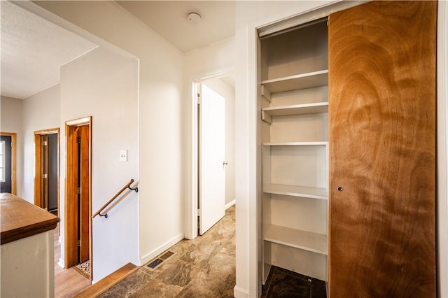 corridor with baseboards, visible vents, and an upstairs landing