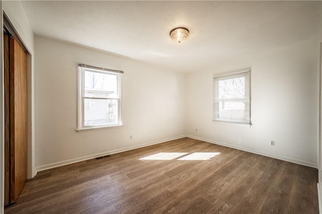 empty room featuring dark wood-type flooring, visible vents, and baseboards