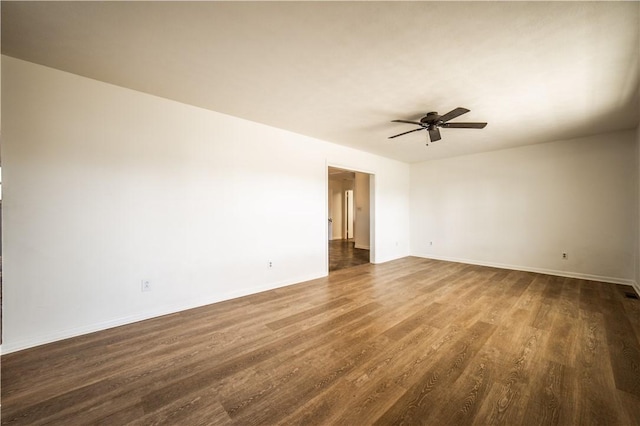 spare room featuring dark wood-style flooring, a ceiling fan, and baseboards