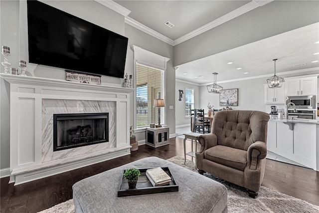 living area featuring dark wood-style floors, visible vents, a premium fireplace, ornamental molding, and baseboards