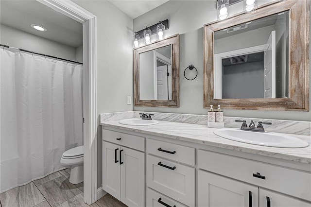 bathroom with toilet, double vanity, and a sink