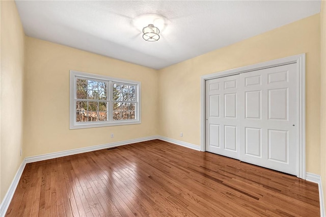 unfurnished bedroom featuring a closet, hardwood / wood-style floors, and baseboards