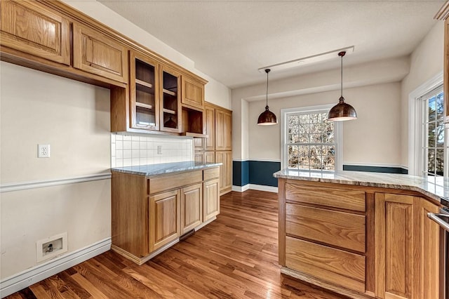 kitchen with glass insert cabinets, brown cabinets, wood finished floors, decorative light fixtures, and backsplash