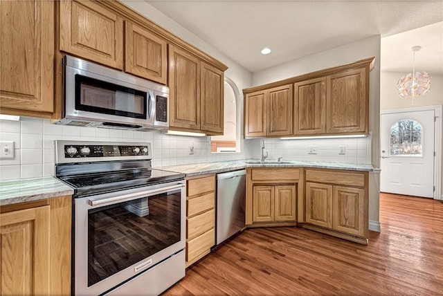 kitchen with stainless steel appliances, backsplash, a healthy amount of sunlight, a sink, and wood finished floors