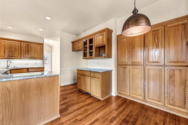 kitchen featuring a sink, wood finished floors, brown cabinets, decorative backsplash, and pendant lighting