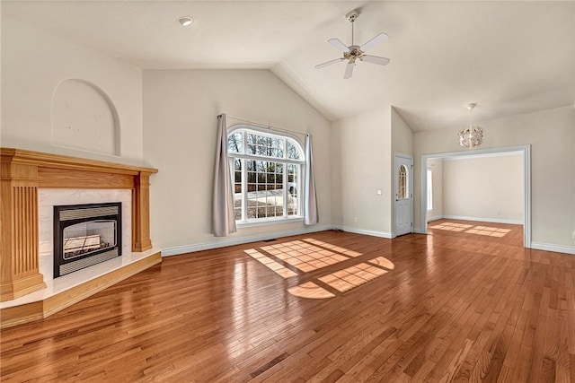 unfurnished living room with hardwood / wood-style flooring, a fireplace, baseboards, and ceiling fan with notable chandelier