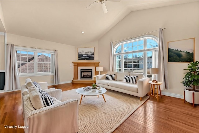 living area with plenty of natural light, wood-type flooring, baseboards, and a fireplace with raised hearth